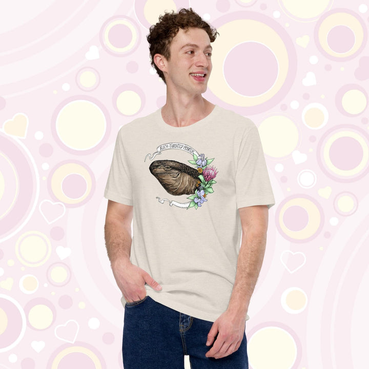 Man wearing a tan colored crew neck tee of a black throated monitor encircled by a banner that reads the species name and with rendered blue and red flowers next to it.