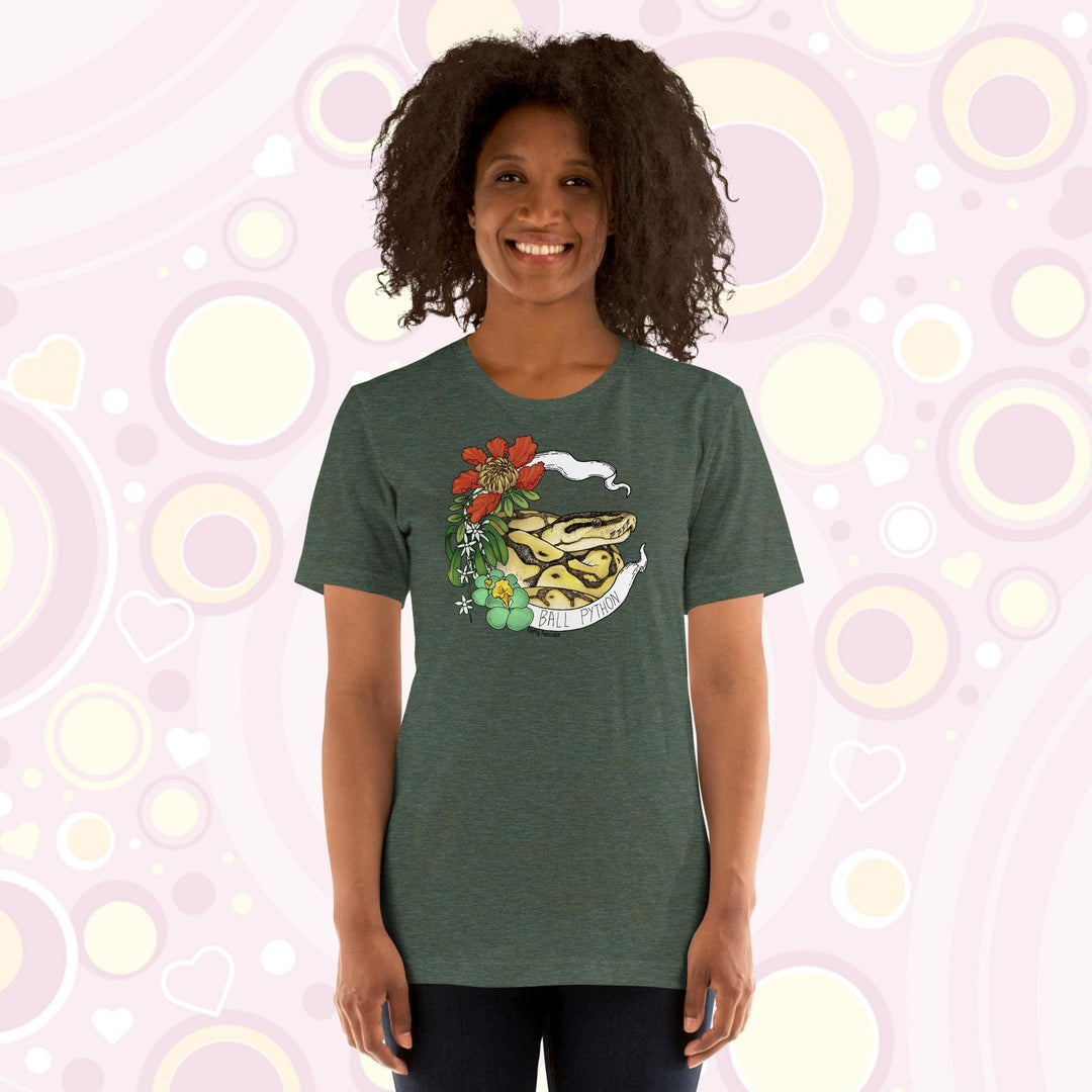 Image shows a woman wearing a heather green crew neck tee with a ball python coiled up in a white banner with the snake species on it. Red, white, and green flowers and plants adorn the left side of the graphic.