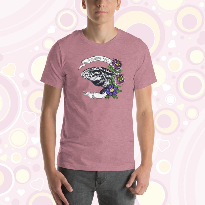 Man wearing pink crew neck tee with a hand drawn graphic of an Argentine Tegu lizard. Purple and pink flowers are on the right of the graphic and a white banner encircles the reptile.