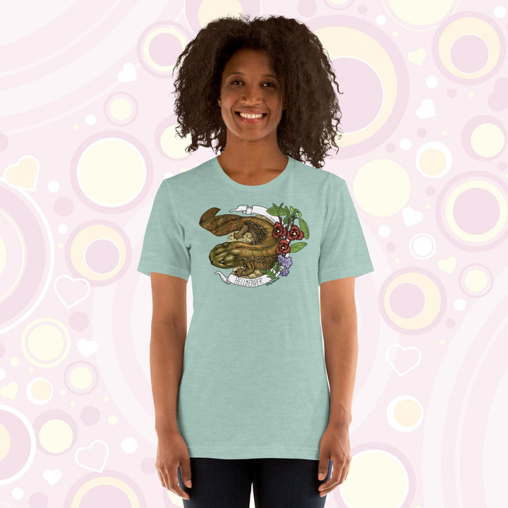 Lady wearing a blue crew neck tee with a hand drawn design of a hellbender amphibian framed by paw paw flowers and a banner that says, "Hellbender".