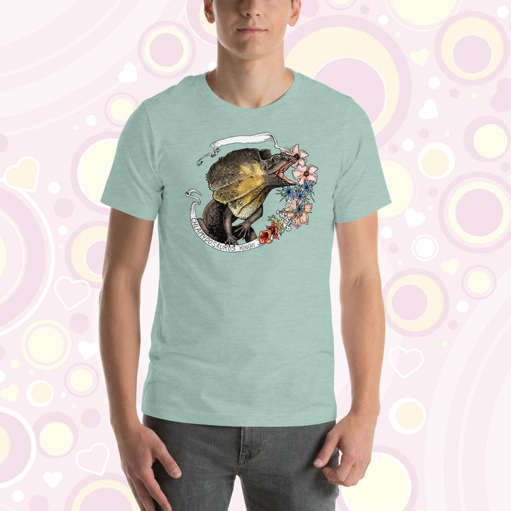 A man wearing a heather prism dusty blue crew neck tee with a frilled lizard from Australia on it. It has a banner with it's species name and pink, blue, and rose colored flowers on the right side.