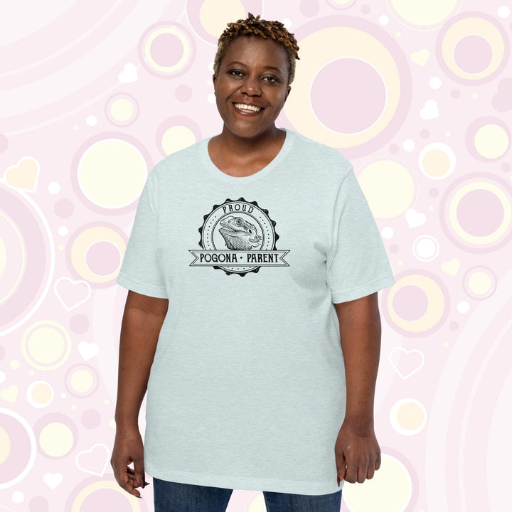 Image of a plus sized woman wearing a heather prism ice blue colored crew neck shirt with a graphic design of a bearded dragon done in black and white centered in a round badge with the text, "Proud Pogona Parent" on the banner design.