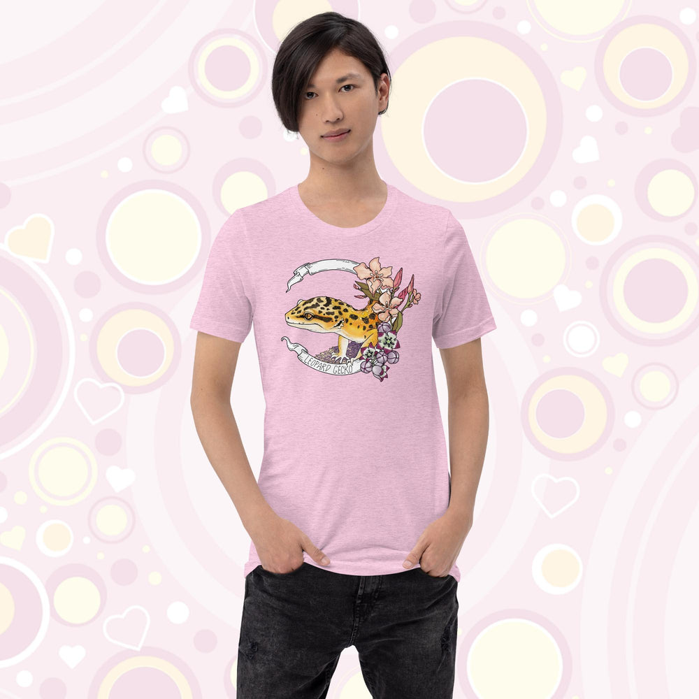 Slim teen wearing heather prism lilac crew neck tee with a leopard gecko art design printed on the front. A white banner encircles the reptile with the species name on it and pink and white flowers are on the right of the design.