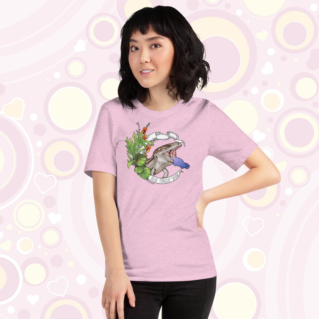 Lady wearing heather prism lilac colored tee with a hand drawn design of a blue tongue skink flashing it's blue tongue in warning. Framed with greenery and a white banner that reads, "Blue Tongue Skink".