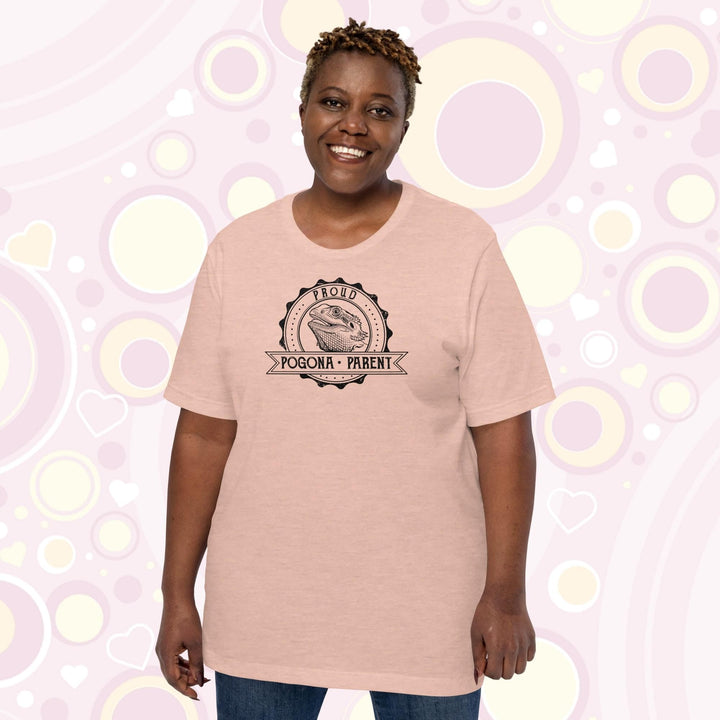 Image of a plus sized woman wearing a heather prism peach colored crew neck shirt with a graphic design of a bearded dragon done in black and white centered in a round badge with the text, "Proud Pogona Parent" on the banner design.