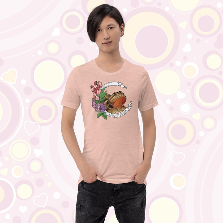 Image of a youth wearing a heather prism peach colored crew neck tee with a bearded dragon on it. The beardie is framed by a white banner with the text, "Bearded dragon" on the bottom and purple and red flowers adorning the left side of the design.