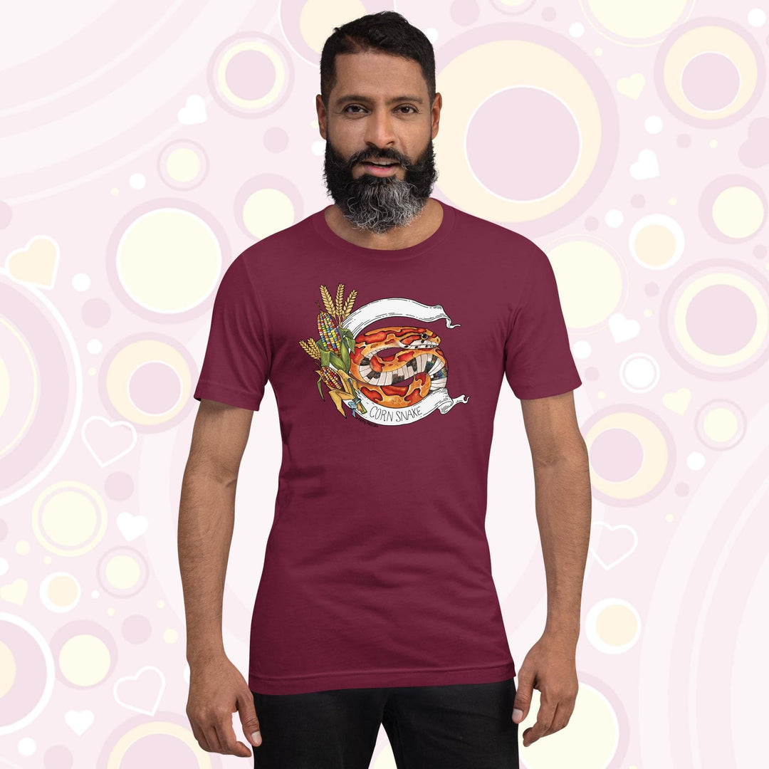 Photo showing a man wearing a maroon crew neck tee shirt with a bright orange and red rat snake with glass corn on the left side and a white banner framing the snake with the text "corn snake" on the bottom.