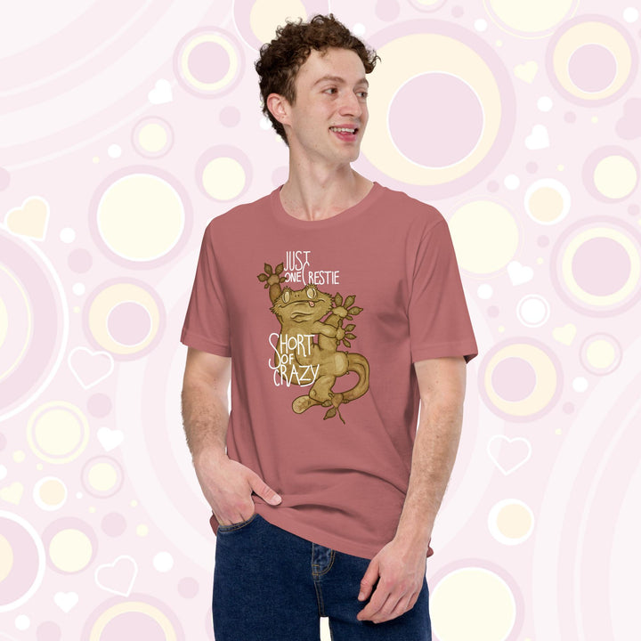 Man wearing mauve crew neck tee with the words "Just one Crestie Short of Crazy" with a crested gecko design clinging to the center. It's legs are flung out and it has a silly expression.