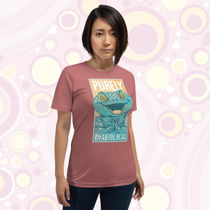 A woman wearing a mauve colored crew neck tee with a large mischievous looking Tokay Gecko smiling and pressing it's feet together. The text Purely Diabolical is split above and below the gecko art.