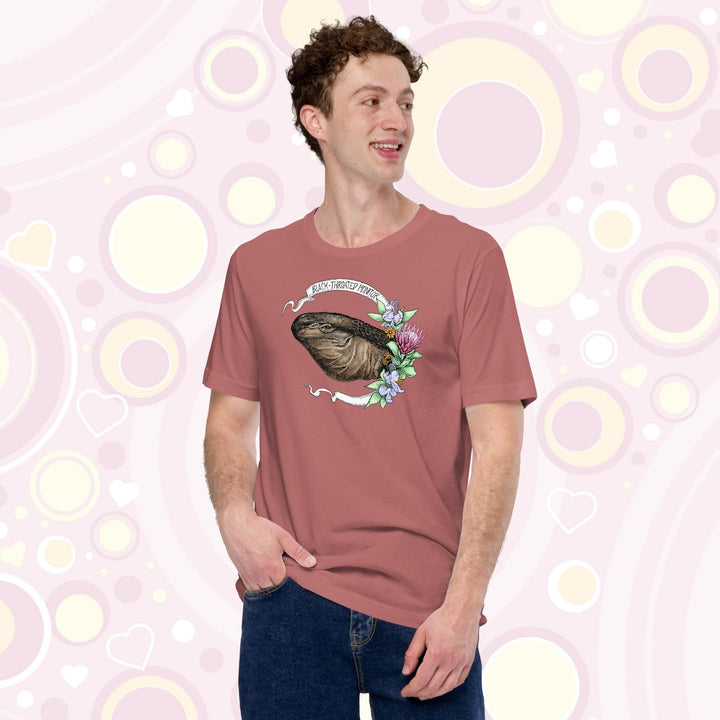 Man wearing a mauve colored crew neck tee of a black throated monitor encircled by a banner that reads the species name and with rendered blue and red flowers next to it.