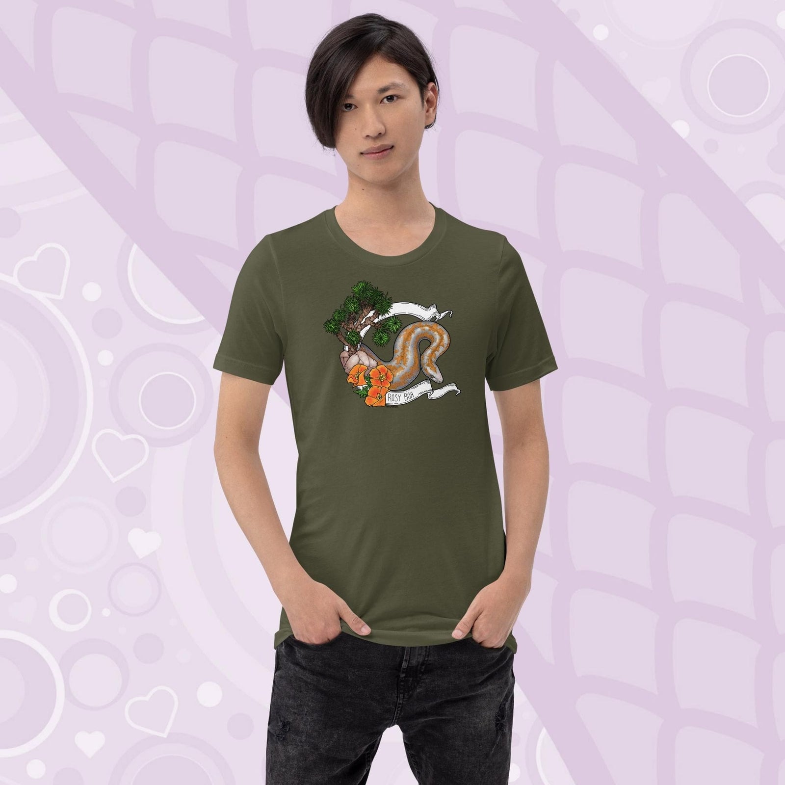 A man wearing a military green colored crew cut tee shirt on a light purple background. The art print on the front is a orange and grey speckled rosy boa snake framed by a white banner with California poppy flowers and a Joshua Tree on the left side of the design. The name Rosy Boa is written on the bottom of the banner.