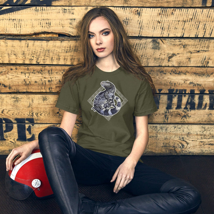 Woman wearing a green t-shirt with a graphic of a black and white tegu coiled around decorative elements in the shape of a diamond, sitting against a wooden wall.