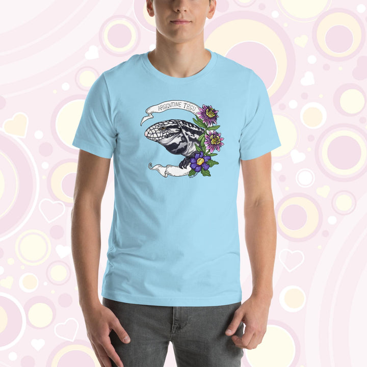 Man wearing blue crew neck tee with a hand drawn graphic of an Argentine Tegu lizard. Purple and pink flowers are on the right of the graphic and a white banner encircles the reptile.