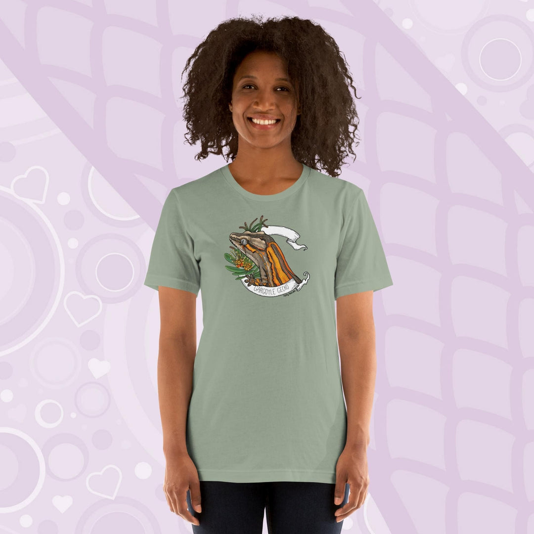 A woman wearing a sage green colored crew neck shirt with an orange striped gargoyle gecko graphic in the middle of the shirt. 