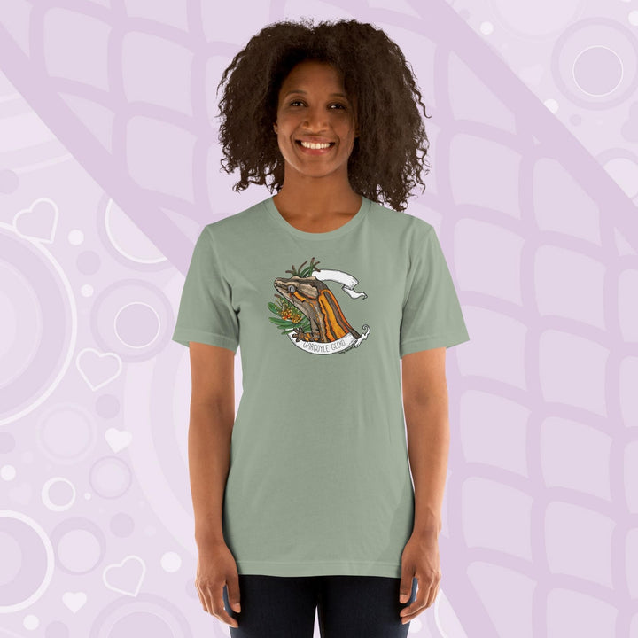 A woman wearing a sage green colored crew neck shirt with an orange striped gargoyle gecko graphic in the middle of the shirt. 