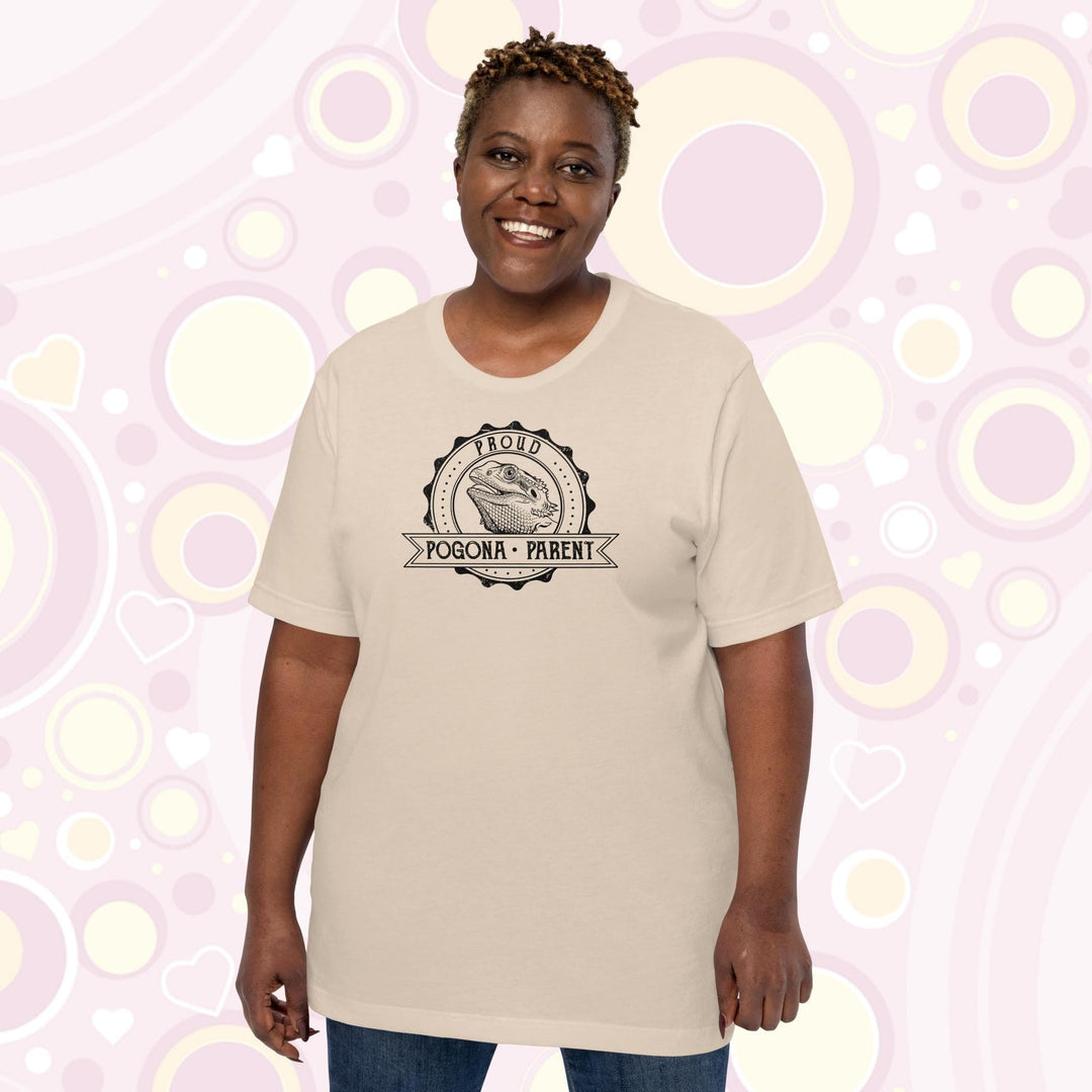 Image of a plus sized woman wearing a soft cream colored crew neck shirt with a graphic design of a bearded dragon done in black and white centered in a round badge with the text, "Proud Pogona Parent" on the banner design.