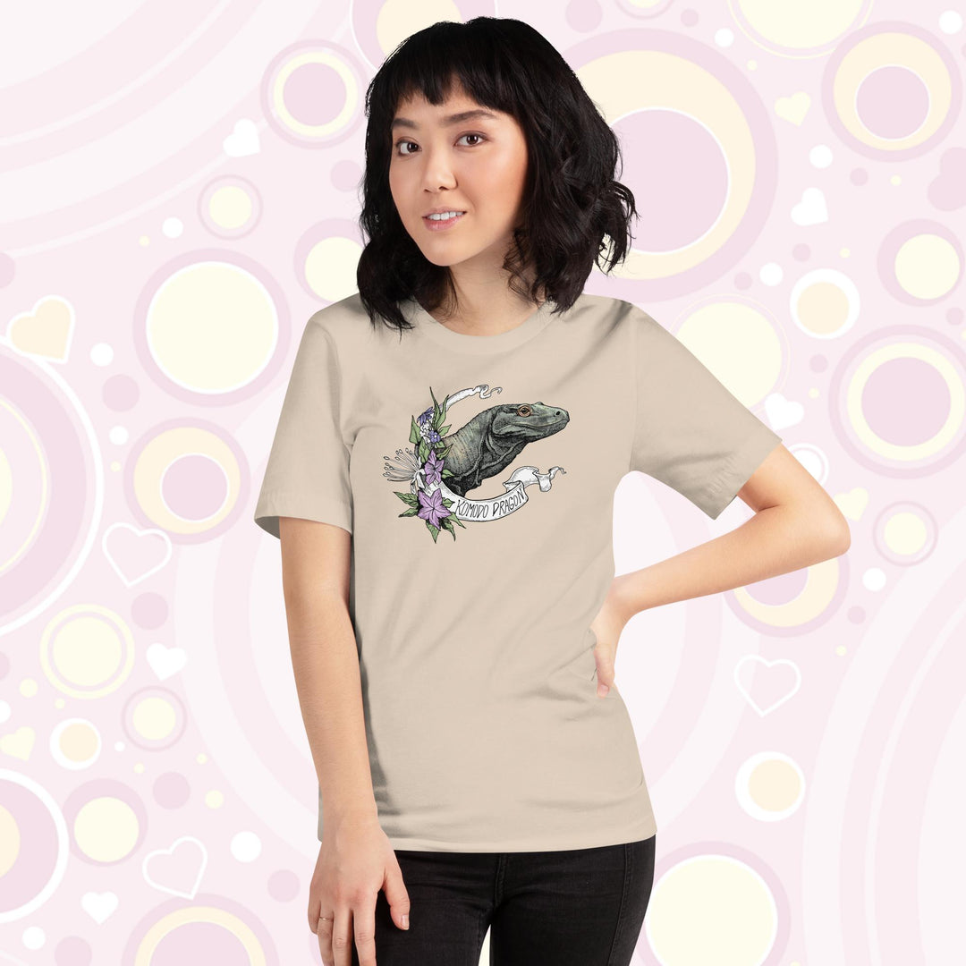 Woman wearing cream colored crew neck tee with a head shot of a komodo dragon lizard framed by purple flowers and a white banner with text of the animal name.