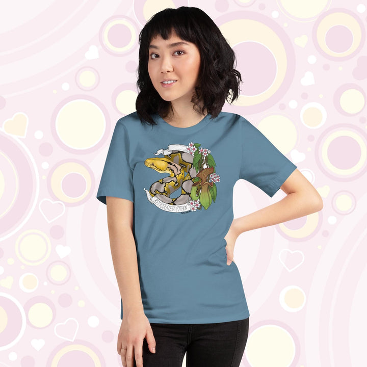 Image of a petite woman wearing a steel blue crew neck tee with a normal phase reticulated python framed by pitcher plants, white flowers, and a white banner with the text, "Reticulated Python" on it.