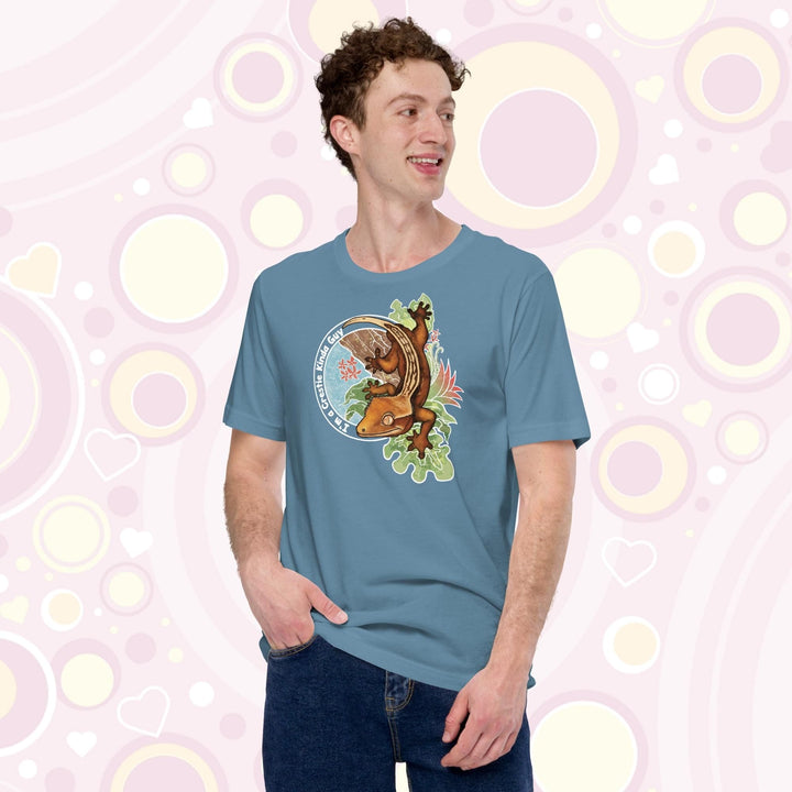 A man wearing a steel blue crew neck tee with a graphic of a crested gecko climbing down from a tree with the words "I'm a crestie kind of guy" on the left hand side.