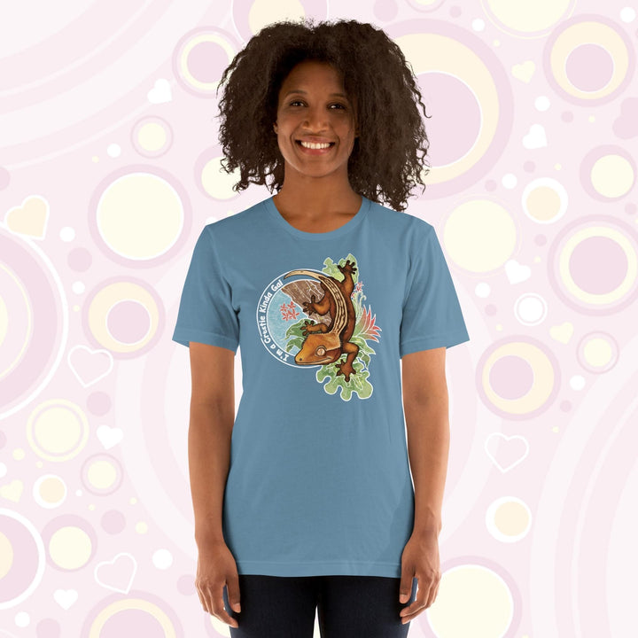 A woman wearing a steel blue crew neck tee with a graphic of a crested gecko climbing down from a tree with the words "I'm a crestie kind of gal" on the left hand side.