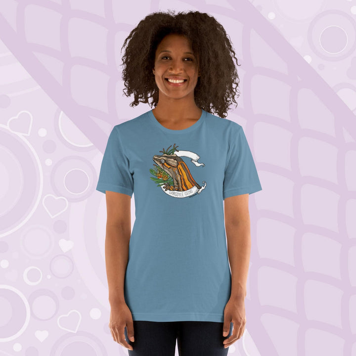 A woman wearing a neutral blue colored crew neck shirt with an orange striped gargoyle gecko graphic in the middle of the shirt. 