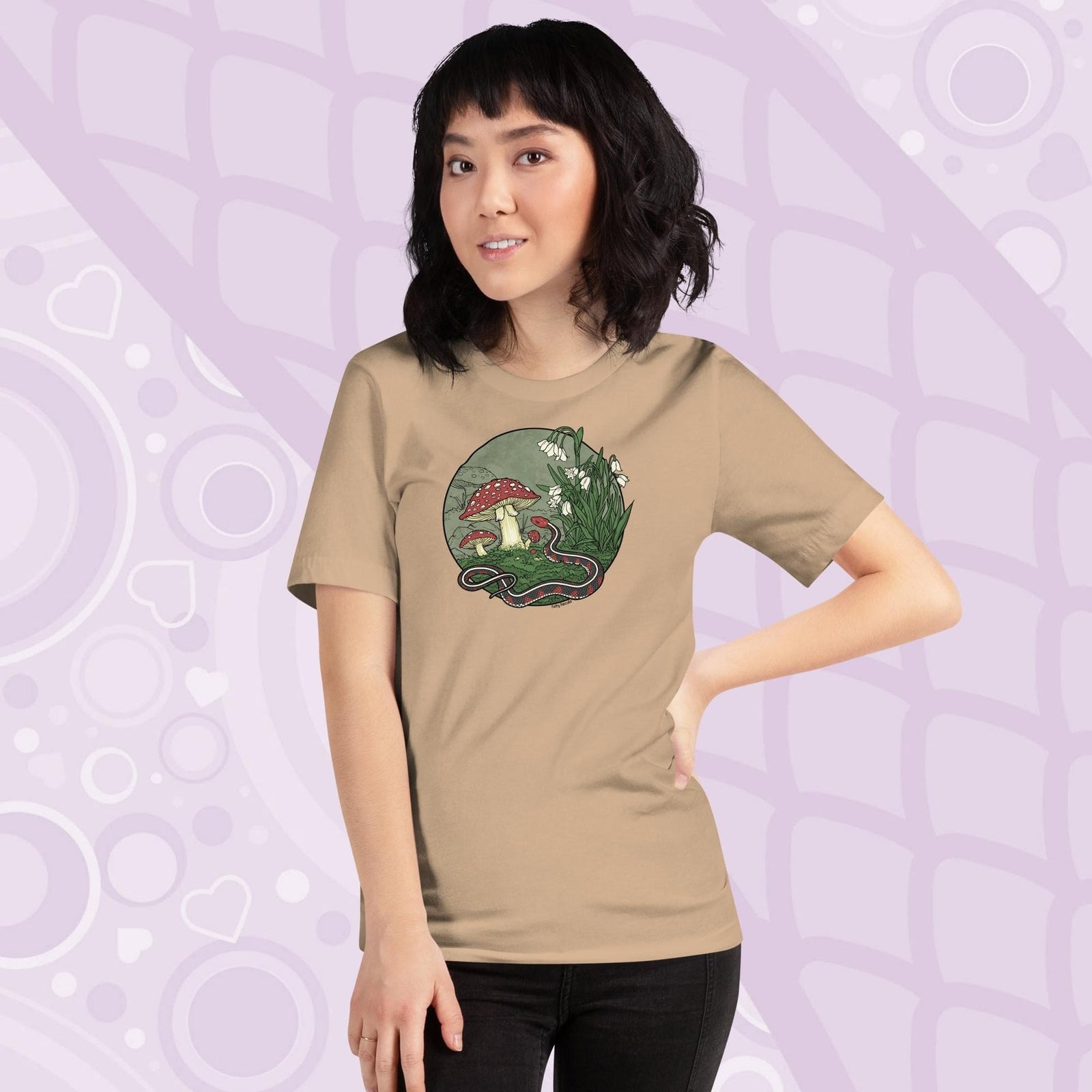 A woman wearing a tan tee shirt with a graphic of a red sided garter snake, surrounded by mushrooms and plants with white blossoms. It has simple colors of red, white, and green.  It has lineart outlining the entire illustration.