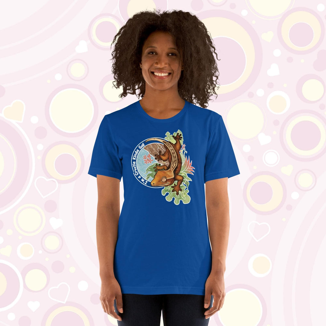 A woman wearing a bright blue crew neck tee with a graphic of a crested gecko climbing down from a tree with the words "I'm a crestie kind of gal" on the left hand side.