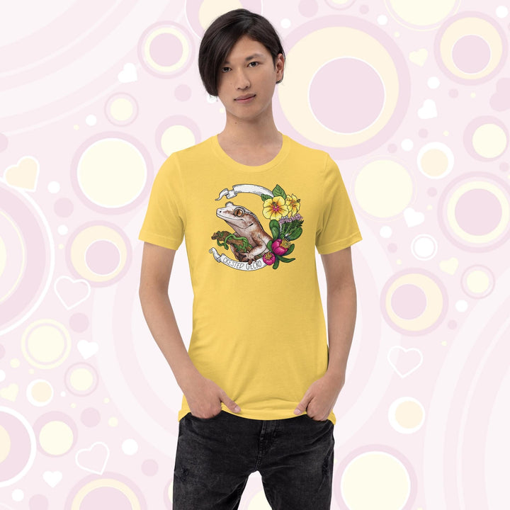 A teen wearing a yellow crew neck tee of a crested gecko holding a branch with yellow hibiscus and other pink flowers as accents along the right of the design. A circular banner reads the name of the animal species on it.