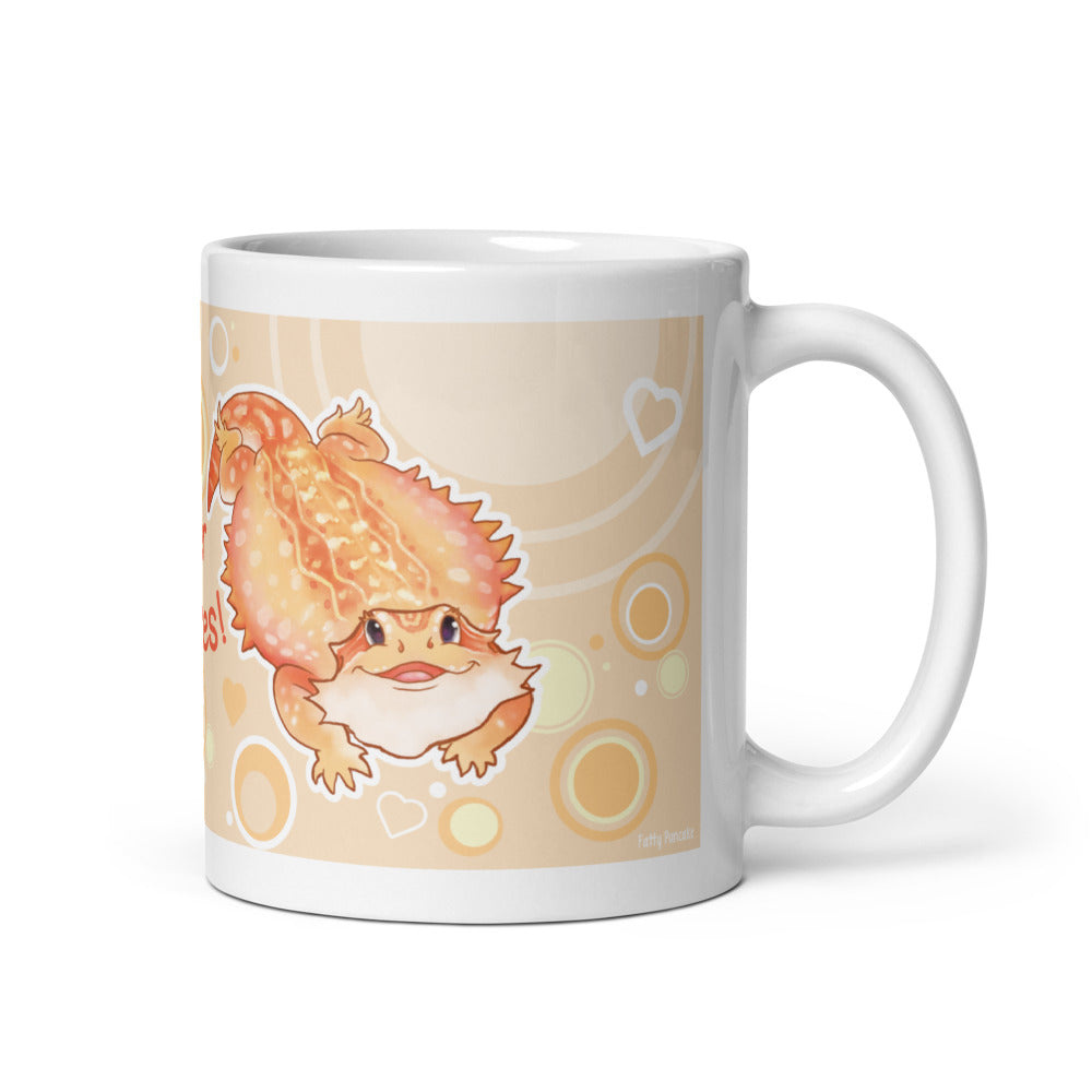 A white ceramic mug featuring a cute cartoon illustration of an orange bearded dragon on a warm cream colored background with circular patterns, shown on a clean white studio background.