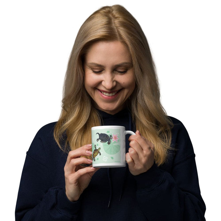 Woman holding a mug with fresh water turtles with lily pads on it against a white background.