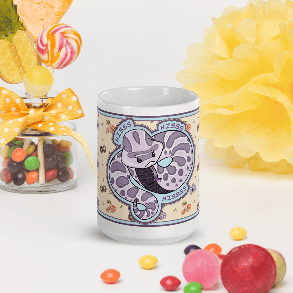 Mug with a hognose snake design printed on it. It's coiled and saying "HISS" multiple times in a dramatic fashion, placed on a white table, and surrounded by colorful candies and flowers on a white background