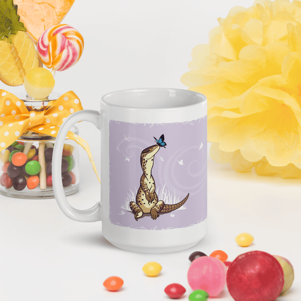 Mug with a lizard design on a purple background, surrounded by colorful candies and flowers.