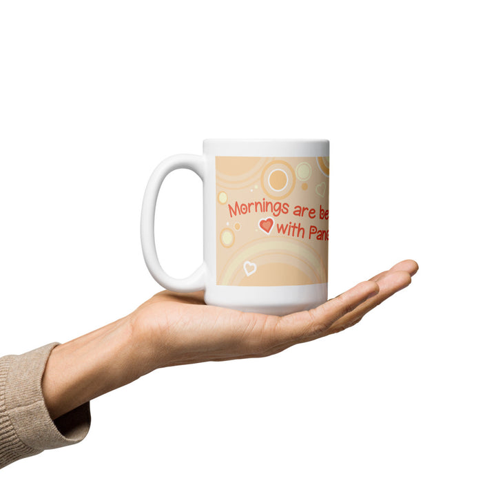 A white ceramic mug held in the palm of a hand with a peach-colored graphic design that reads &