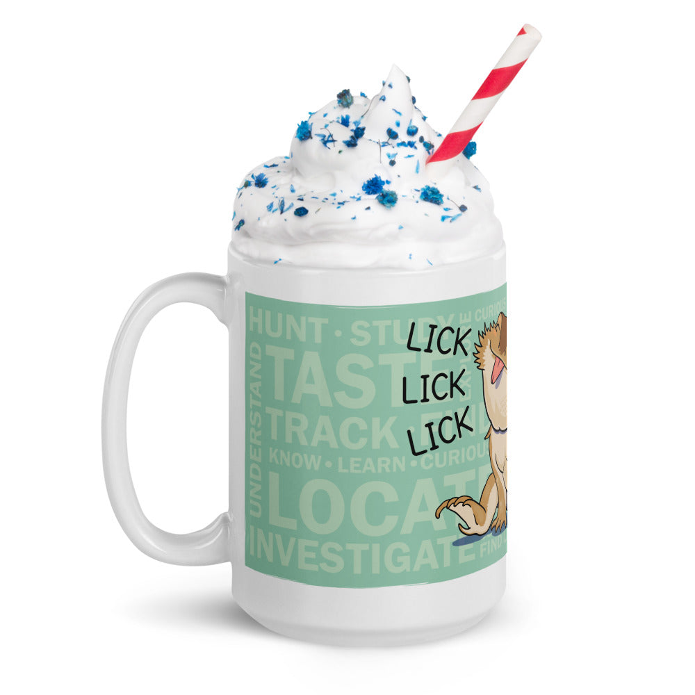 A white ceramic mug featuring a light green background with the words HUNT, TASTE, TRACK, KNOW, LEARN, CURIOUS, LOCATE, INVESTIGATE, and UNDERSTAND. A cartoon dog is shown with the text LICK LICK LICK, topped with whipped cream and a red-and-white straw.