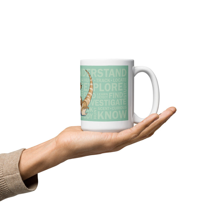 A hand holding a ceramic mug in the palm that is a mint color and has many words in the background like, "explore, understand, track, know, investigate" and more.