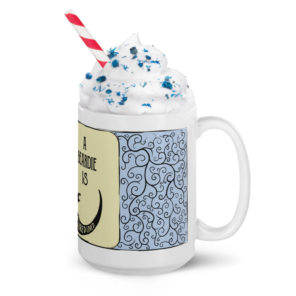 A white ceramic mug featuring a light yellow panel with black text and a light blue section with a black swirling vine pattern. The mug is filled with white whipped cream topped with blue sprinkles and a red and white striped straw.
