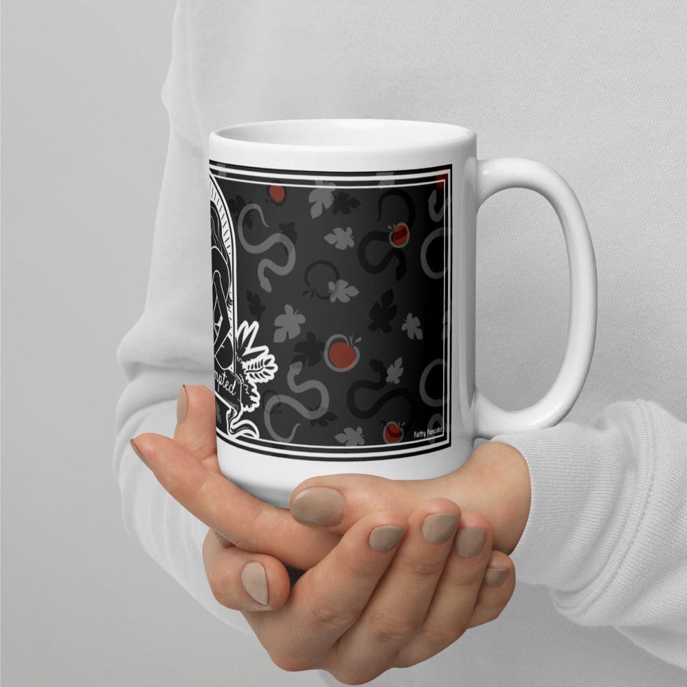 A hand holding a grey patterned mug with apples and snakes and leaves.