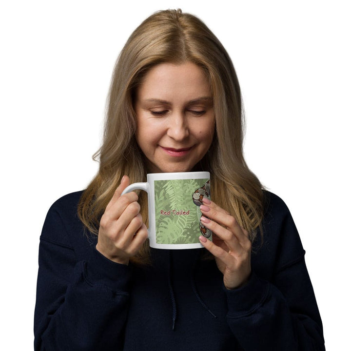 A woman holding a white ceramic mug featuring a graphic illustration of a brown and tan boa constrictor snake coiled against a green background with a fern leaf pattern. The text "Boa Constrictor" is printed in red letters on the side of the mug.