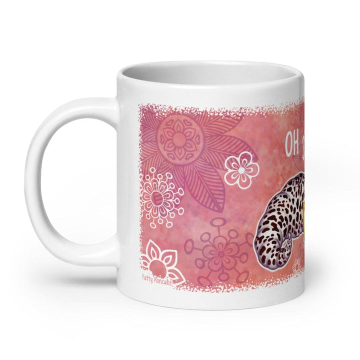A white ceramic mug featuring a pink and coral watercolor-style floral print with a leopard gecko tail  illustration and partial text, shown on a clean white background. The handle is on the left.