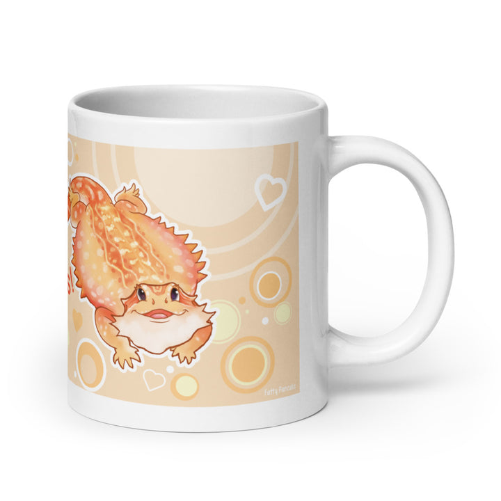A white ceramic mug featuring a cartoon illustration of an orange and yellow bearded dragon on a beige background with circular patterns, shown on a clean white studio background.