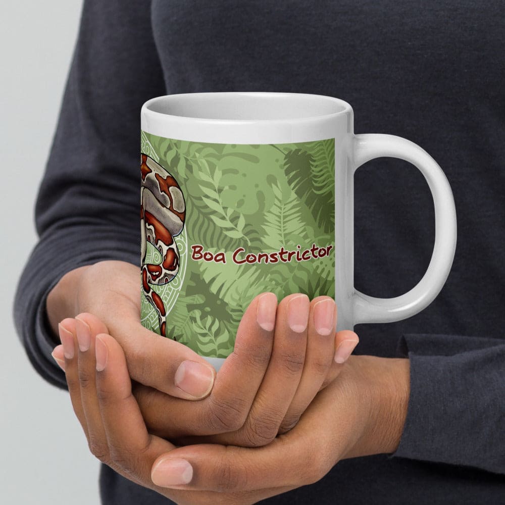 A hand holding a mug with a green plant background with the name Boa Constrictor labeled on the side.