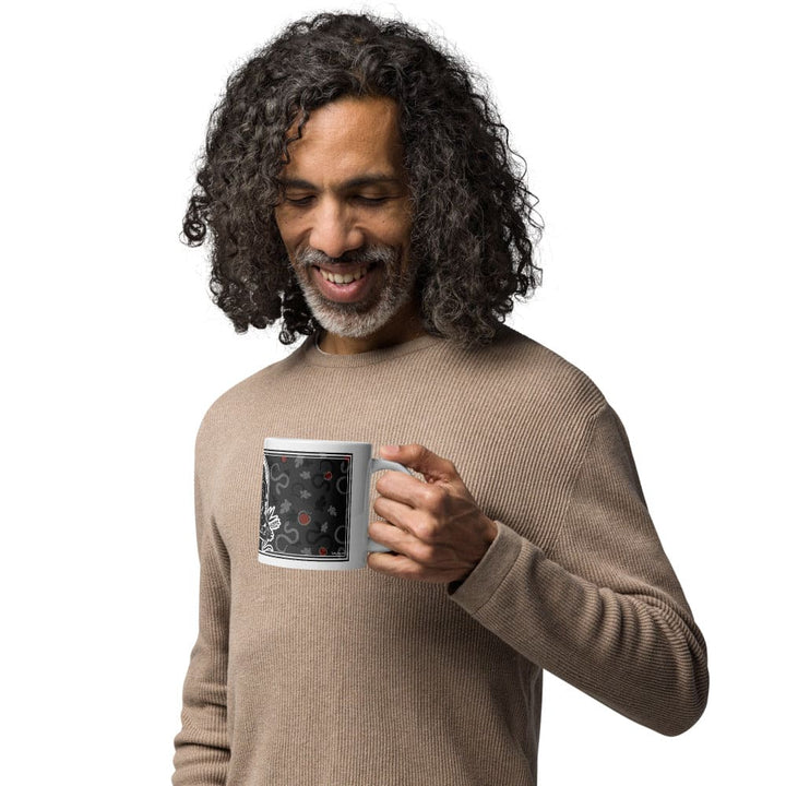 A man holding a grey mug with a snake, leaf, and apple pattern on it.