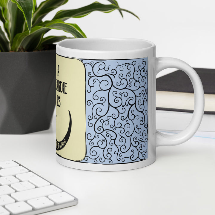 A blue and cream mug sitting on a white table with a keyboard and plant in the background.